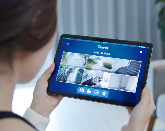 Access Control Systems Person monitoring live security camera feeds on a tablet using a home surveillance app.