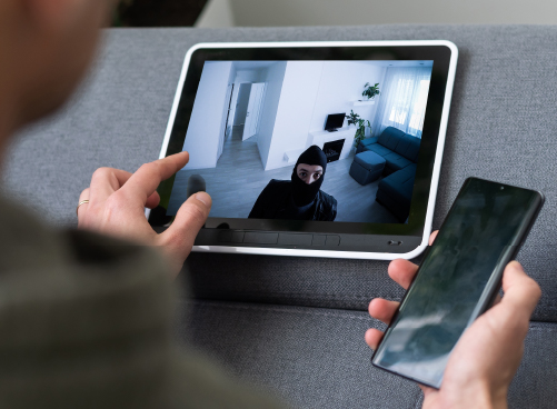 Alarm Monitoring & Response Services Person viewing a tablet showing live security camera footage of an intruder inside a home.
