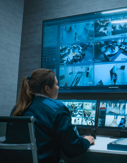 Electronic Article Surveillance (EAS) Security officer monitoring multiple surveillance camera feeds on large control room screens.