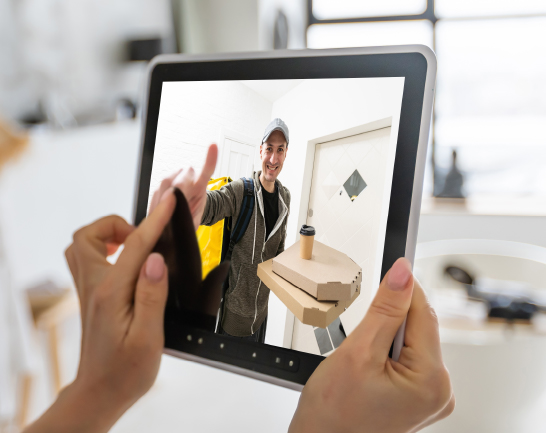 Integrated Electronic Security Solutions Person using a tablet to view a delivery driver holding food and drinks at the front door through a security camera.