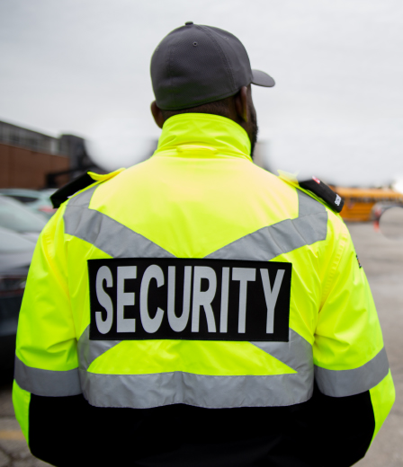 Mobile Patrol - Our Mobile Patrol Services A close-up side profile of a male Victoria Police officer standing in a line with other officers. He is wearing a dark blue uniform, a checkered baseball cap, and safety glasses. A police patch is visible on his shoulder. Other officers, some wearing face masks, are standing in the background.