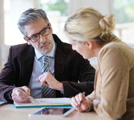 Comprehensive Quality and Safety Systems A professional man and woman sitting at a desk engaged in a serious discussion, reviewing documents and notes together in an office setting.