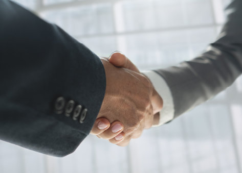 Customer Success and Retention Close-up of two people in business attire shaking hands in a bright office setting, symbolizing partnership or agreement.
