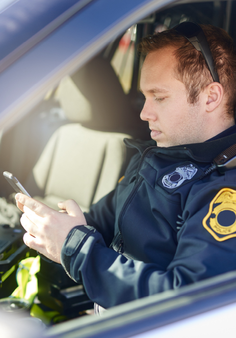 Emergency Response and Incident Management A uniformed security officer sitting inside a vehicle, focused on using a smartphone, possibly coordinating or reporting an incident.