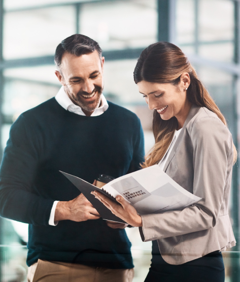 Proven Track Record Across Australia Two business professionals smiling and reviewing documents together in a modern office environment, representing a successful partnership and proven track record.